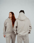 Back view of two models wearing matching Brklyn Park Essence fleece hoodies and sweatpants in neutral beige