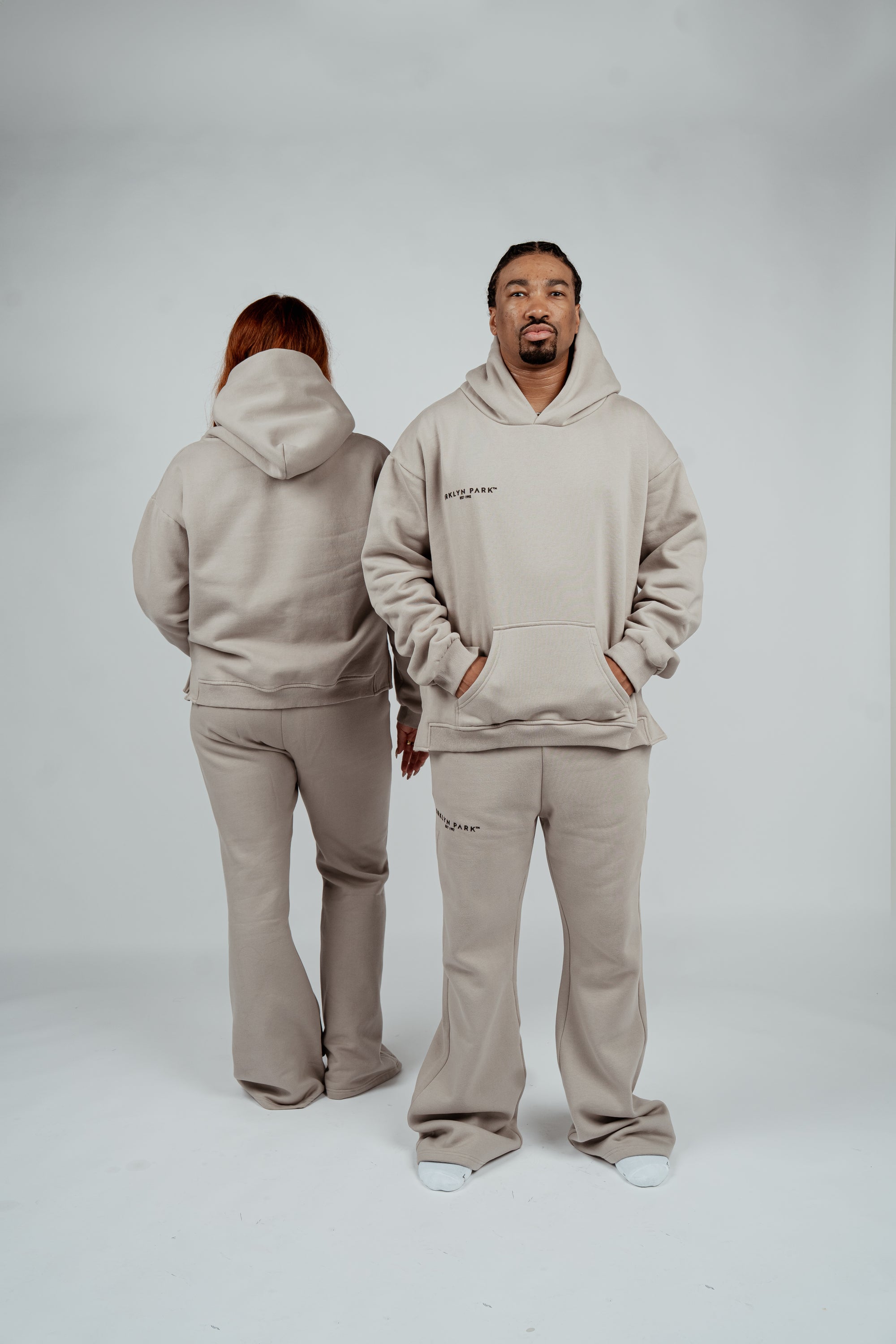 Unisex models wearing Brklyn Park Essence Fleece Sweat Sets featuring gray heavyweight sweatpants and hoodies in minimalist style