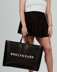 A person holding a large black leather tote bag with 'BRKLYN PARK' printed in white on the side.