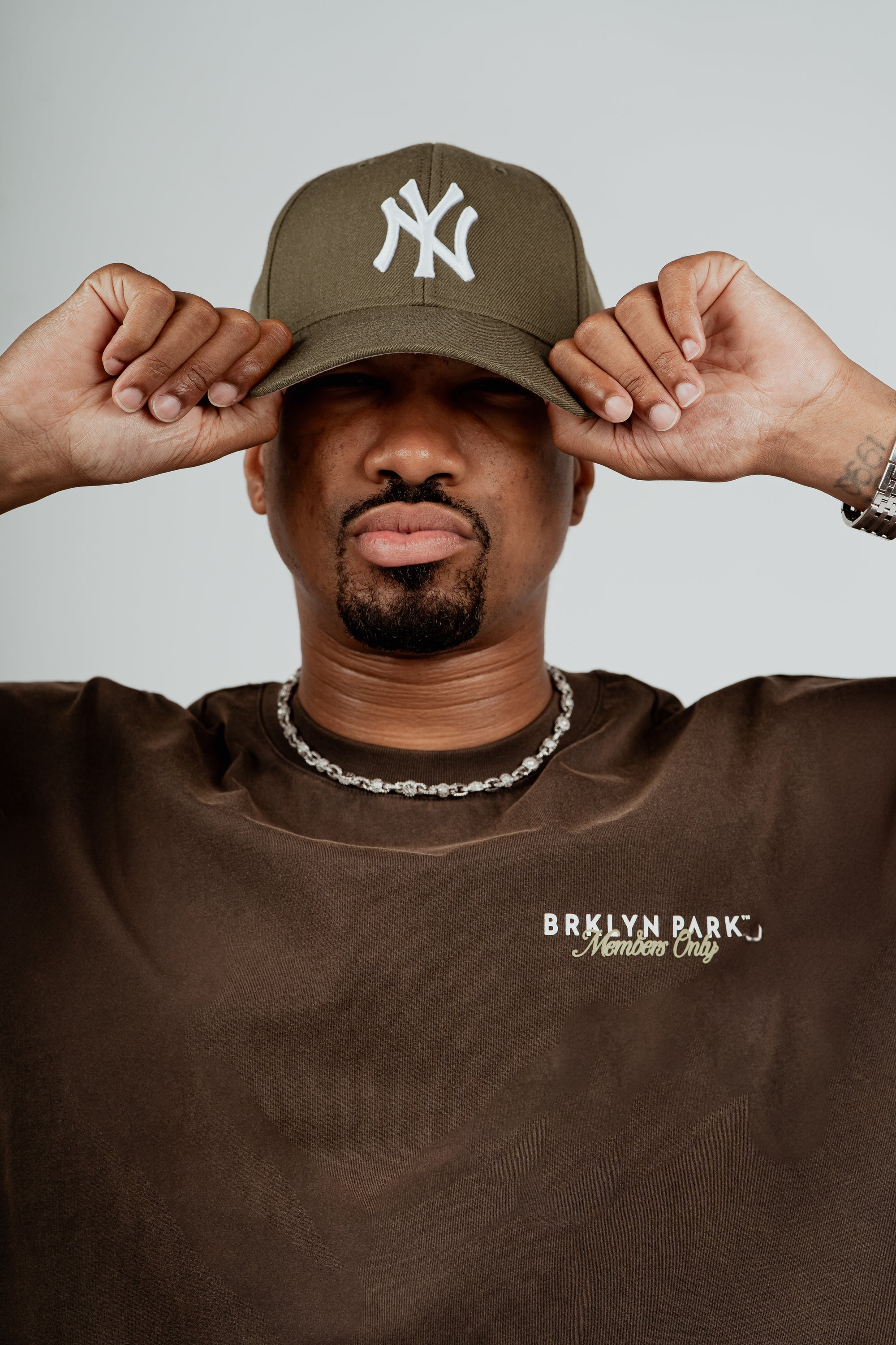 Brklyn Park Members Only brown t-shirt styled with chain necklace and green New York Yankees cap